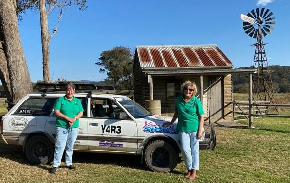 Stadning in front of their car and an outback hut