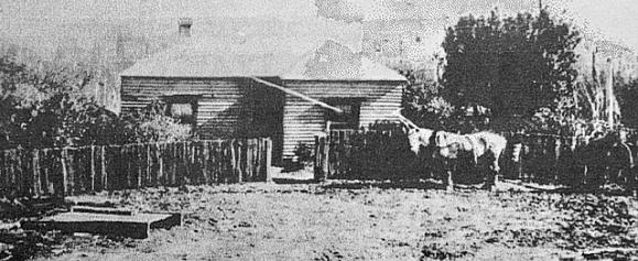 Weatherboard house with rough picket fence and horse outside